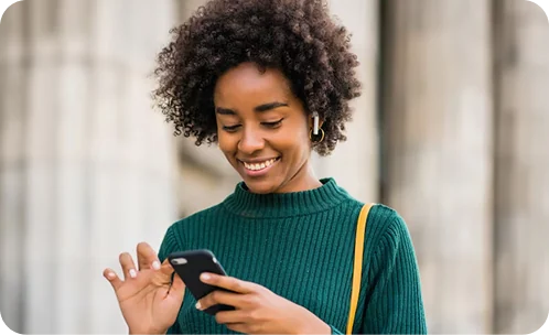 A woman in a green knit smiling at her phone on a city street
