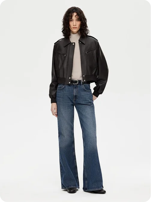 A woman in a black leather bomber over a beige mock neck with wide-leg blue jeans