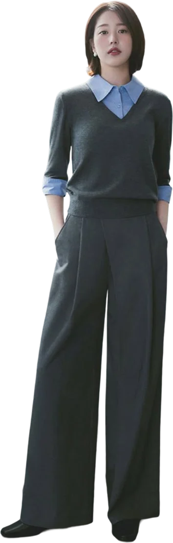 A woman in a charcoal V-neck knit over a blue collared shirt, with charcoal wide-leg pleated trousers