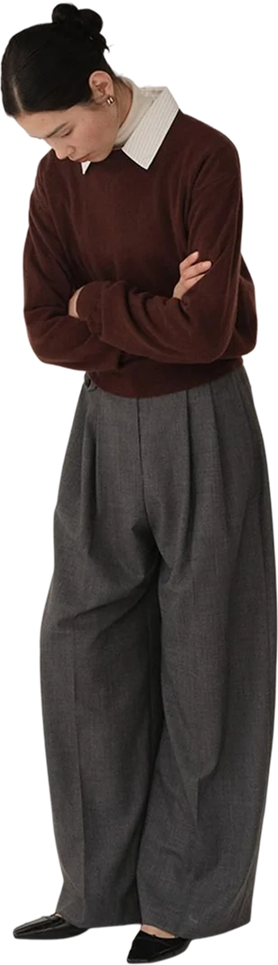 A woman in a chocolate-brown knit over a white collared shirt, with charcoal wide-leg pleated trousers