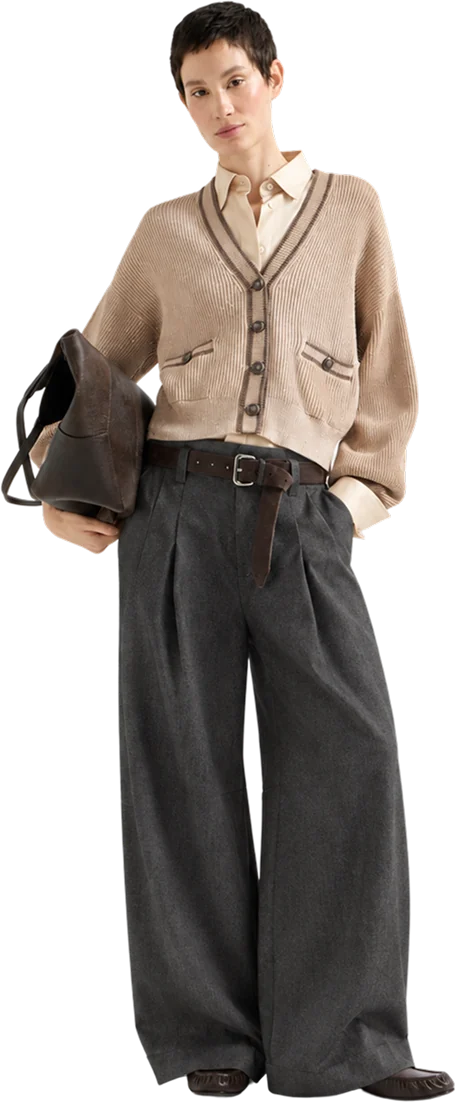 A woman in a beige ribbed cardigan over a beige shirt, with charcoal wide-leg pleated trousers, holding a bag